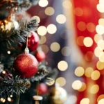 Sapin de Noël décoré avec des boules rouges et dorées, entouré de lumières floues créant une ambiance festive et chaleureuse.