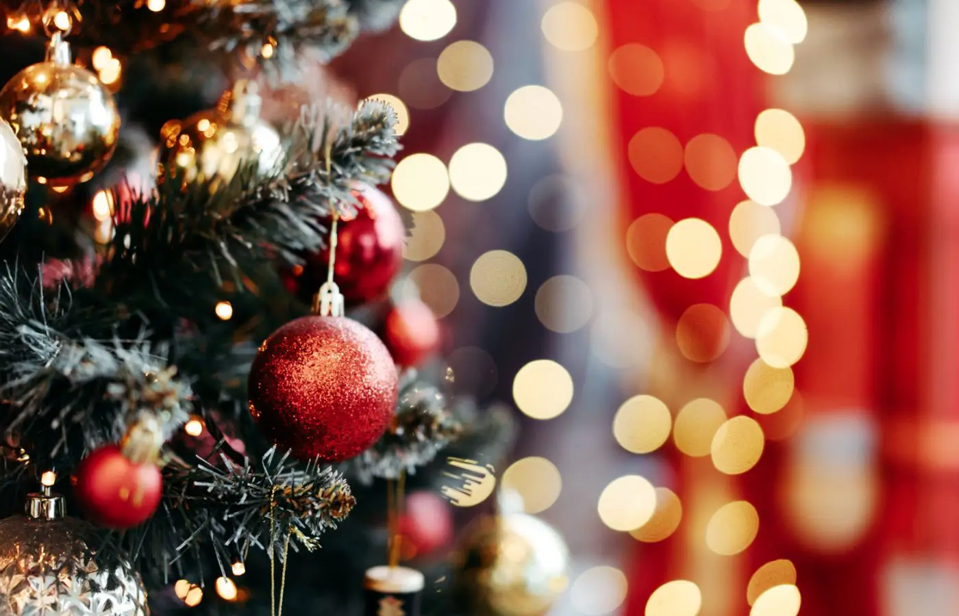 Sapin de Noël décoré avec des boules rouges et dorées, entouré de lumières floues créant une ambiance festive et chaleureuse.