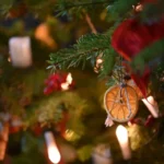 Détail d'une décoration naturelle de Noël avec tranches d'orange séchées et guirlandes lumineuses sur un sapin.