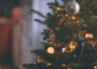 Sapin de Noël décoré avec des lumières et des ornements, dont une petite chaussette portant l'inscription 'Noël', dans une ambiance chaleureuse.